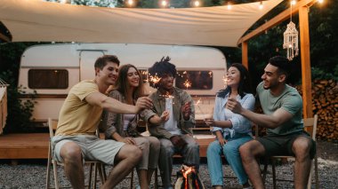 Milenyum çeşitliliği olan arkadaşlar, yanan maytaplarla şenlik ateşinin yanında oturuyor, eğleniyor, kamp gezisinde birlikte bir şeyler kutluyor, karavanda seyahat ediyor, dışarıda dostça sohbetin tadını çıkarıyorlar.