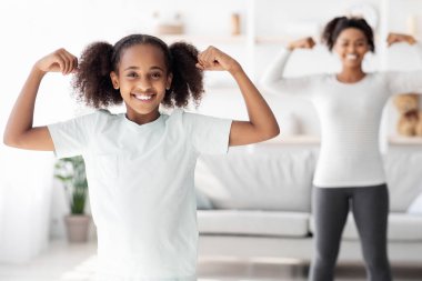 Spor giyim kuşamında sportif giyinen neşeli siyah kız, sevimli atletik Afrikalı Amerikalı çocuk evde annesiyle egzersiz yapıyor, oturma odasının içinde. Sağlıklı aile hayatı, spor anlayışı