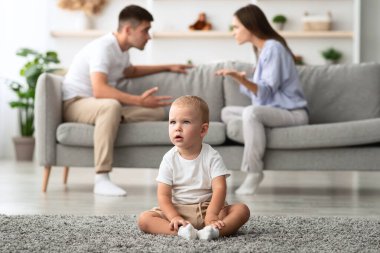 Aile Çakışmaları Konsepti. Küçük bebek tek başına otururken ebeveynler arka planda tartışıyor, genç adam ve kadın bebeklerini tartışıyor ve görmezden geliyor, seçici bir şekilde yeni yürümeye başlayan çocuğa odaklanıyor, boş alan yaratıyor.