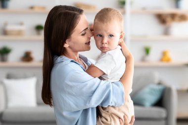 Anneler Bakım Konsepti. Güzel ve genç bir kadın, sevimli bebeğini ellerinde tutuyor, annesini seviyor, tatlı bebeğini kucaklıyor, evde dinleniyor, birlikte vakit geçiriyorlar, boşluğu kopyalıyorlar.