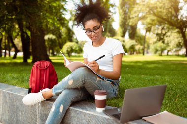 E-öğrenme. Afro-Amerikalı Kız Hazırlık Dersi Laptop kullanıyor ve dışarıda park yerinde notlar alıyor. Modern Uzaklık Eğitimi ve Çevrimiçi Öğrenim Kavramı