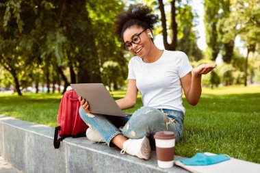 E-öğrenme. Bilgisayarı kullanan mutlu Amerikalı öğrenci dışarıda oturarak uzaktan eğitim veren bilgisayar araması yapıyor ve sanal ders veriyor. Uzaktan Üniversite Eğitimi. Teknoloji ve Öğrencilik