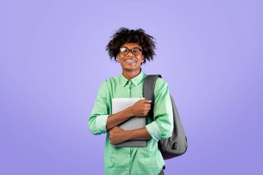 Öğrencilerin yaşam tarzı konsepti. Mutlu Afro-Amerikalı adam dizüstü bilgisayarını tutuyor, mavi stüdyo arka planında duruyor. E-öğrenme ve eğitim araçları, uzak online çalışma