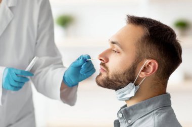 Kapsamlı tanı prosedürü. Doktor, evde steril bez çubuğu kullanan beyaz bir adam için nazal PCR testi yapıyor. Milenyum adamı koronavirüs analizinden geçiyor, sağlık kontrolü yapıyor.