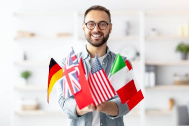 Modern eğitim ve öğrenci değişimi. Evinde bir sürü farklı bayrak tutan neşeli beyaz bir adam. Mutlu milenyum adamı yabancı dil okulunun reklamını yapıyor, yurtdışına göç ediyor.