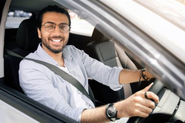 Yakışıklı, şık, orta doğulu bir adam güzel bir araba kullanıyor, arabanın camından bakıyor ve kameraya gülümsüyor, ofise gidiyor ya da tek başına seyahat ediyor, yakın plan fotoğraf, uzay kopyası.