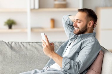 Yakışıklı milenyum çocuğu koltukta cep telefonuyla rahatlıyor, gülümsüyor ve evde arkadaşına mesaj atıyor. Genç beyaz adam mesaj yazıyor, görüntülü konuşma yapıyor ya da evde internet yayıyor.