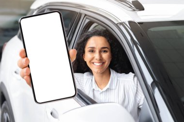 Yeni model beyaz bir arabada oturan, kameraya gülümseyen, internetten araba kiralayan, akıllı telefon kullanan, pozitif milenyum ortadoğulu bir kadın. Araba galerisi çevrimiçi