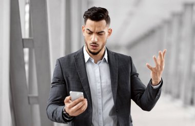 Endişeli Arap iş adamının portresi, havaalanı terminalinde beklerken akıllı telefondan mesaj okuyor, cep telefonu ekranına bakan endişeli Orta Doğulu adam, kötü haberlere duygusal tepki veriyor.