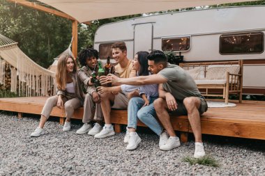 Kamp gezisinde bira içen, şişelerle kadeh kaldıran, dışarıda eğlenen neşeli, çok ırklı genç arkadaşlar. Milenyum halkı yaz tatilinde karavan yakınlarında parti veriyor