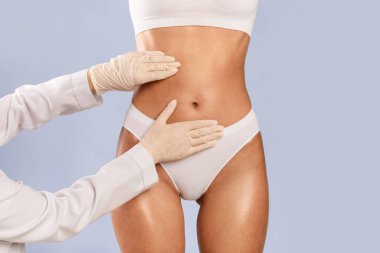 Mükemmel Vücut yapmak. Plastik cerrahi kliniğinde muayene olan tanınmayan genç bir kadın karın ve doktorların karın yağlarına dokunup muayene ettikleri yakın çekim görüntüsü.