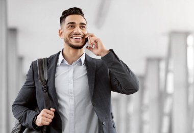 Havaalanı terminalinde yürürken cep telefonuyla konuşan gülümseyen Orta Doğulu adam, mutlu Arap iş adamı el bagajı taşıyor ve cep telefonuyla keyifli sohbetler yapıyor.