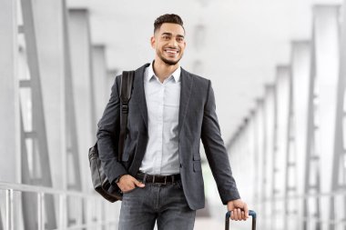 Havalimanında çantasıyla yürüyen yakışıklı bir Arap 'ın portresi, günlük kıyafetlerle gezen genç bir Orta Doğulu' nun gülümsemesi, yaklaşan hava yolculuğunun tadını çıkarması, kopyalama alanı.