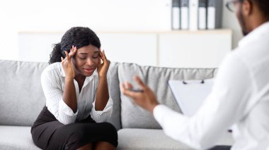Stresli genç zenci bayan ofisteki psikoloğa danışmak için şakaklarını ovalıyor. Depresyon ya da PTSD 'den muzdarip Millennial Afro kadın, profesyonel yardım arıyor