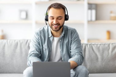Kulaklıklı, gülümseyen beyaz bir adam evde bilgisayarla video görüşmesi yapıyor ve web kamerasıyla konuşuyor. Milenyum adamı internet üzerinden iletişim kuruyor, web konferansına katılıyor veya uzak bir toplantıya katılıyor
