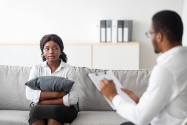 Psikoterapist danışmanlık klinikte terapi gören Afrikalı Amerikalı bayanı üzdü. Psikolojik sorunları olan genç siyahi kadın danışmanlık ofisinde kanepede yastığa sarılıyor.