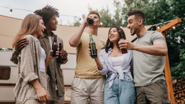 Kamp gezisinde bira içen, sohbet eden, şakalaşan ve dışarıda birlikte gülen çok ırklı genç insanlar. Bin yıllık çeşitli arkadaşlar yaz tatilinde karavanın yanında alkolle parti yapıyorlar.