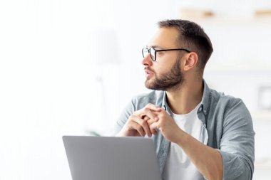 Sıkıcı genç adam dizüstü bilgisayarın yanında oturuyor, yan tarafa bakıyor, hayal kuruyor, internet üzerinden çalışırken bir şeyler düşünüyor. Milenyum Kafkas 'lı sıkıcı uzaktan kumandalı bir adam