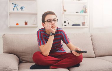 İzleyecek ilginç bir şey yok. Üzgün ve düşünceli genç bir çocuk uzaktan kumanda tutuyor ve televizyon izlerken sıkılmış görünüyor.