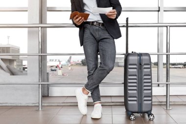 Havaalanı Terminali 'nin yanında bavul başında dururken biletlerdeki uçuş süresini kontrol eden tanınmayan adam, erkek yolcu uçuşu için bekliyor, gezintiye hazır, kesilmiş resim, boş alan