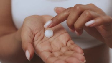 Genç bir Afrikalı Amerikalı kadın evde kendini şımartmaktan hoşlanır. Eline az miktarda cilt bakımı ürünü sürüyor. Güzellik bakımına odaklanıyor..