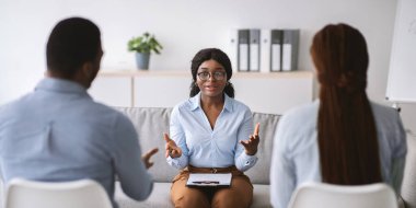 Evlilik terapisi konsepti. Siyahi kadın psikolog klinikte genç evli bir çiftle seans yapıyor. Afro-Amerikalı eşler ofiste psikoterapist eşlere danışmanlık yapıyor, afiş tasarımı