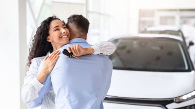 Yepyeni arabasının anahtarıyla kendinden geçmiş genç kıvırcık kadın. Sevgi dolu kocasına sarılıyor ve gülümsüyor. Minnettar ve mutlu hissediyor.