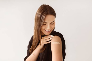 Gribi önleme ve tedavi etme. Beyaz kadın hasta arka planda antiviral aşıdan sonra omzuna yara bandı yapıştırmış. Dokunulmazlık