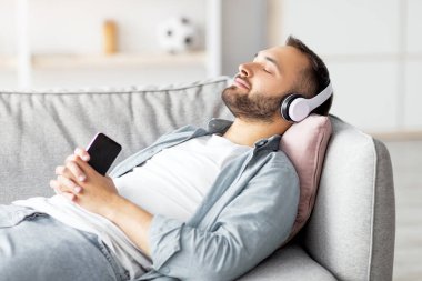 Rahat genç adam, kulaklıkla koltukta uzanıyor, akıllı telefondan müzik dinliyor, yeni mobil uygulama kullanıyor, maket yapıyor. Sakin Kafkasyalı adam evde popüler bir şarkı ya da sesli kitaptan hoşlanıyor.