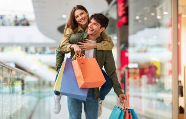 Mutlu eşler alışveriş yapıyor ve eğleniyor, koca eşini sırtında taşıyor ve hafta sonları modern hipermarkette renkli alışveriş torbaları tutuyor. Büyük Mevsimlik Satış ve Ticaret Konsepti