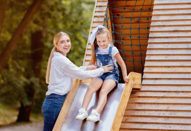 Anne, kaydırağın altında birlikte zaman geçirip dışarıda oyun oynarken mutlu bir anne. Boşluğu Kopyala