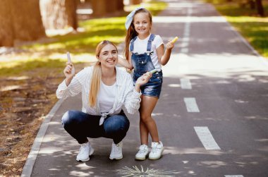 Anne ve Kız Poz Veren Chalks Şehir Parkı 'nda çizim yapıyor. Hafta sonu tatili ve aile eğlencesi. Boşluğu Kopyala