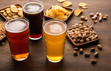 Arkadaşlara göre bir masa. Çıtır çıtır atıştırmalıklar ve farklı tipte biralar, ahşap arka planda, yakın plan.