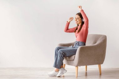 Koltuğunda oturan, müzik dinleyen, el kaldıran, havalı şarkılar eşliğinde dans eden, beyaz stüdyo duvarına karşı popüler film müziğinin keyfini çıkaran,