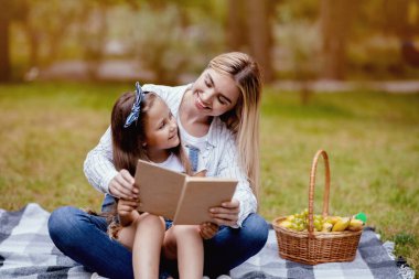 Küçük kızım, Anne Haftasonunu Park 'ta Geçiren En İyi Kitap' ı okuyor. Aile Pikniği