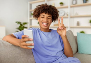 Kanepede oturup selfie çeken ya da cep telefonuyla video görüşmesi yapan acayip siyahi bir genç. Pozitif Afro ergen kendini fotoğraflıyor, arkadaşlarıyla internetten sohbet ediyor, modern aletler kullanıyor.