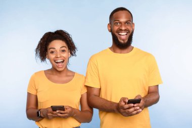 Çevrimiçi yaşam konsepti. Milenyum Afro-Amerikan çifti cep telefonu kullanıyor, internet ya da sosyal medyayı kontrol ediyor. Heyecanlı adam ve kadın ellerinde modern aletlerle