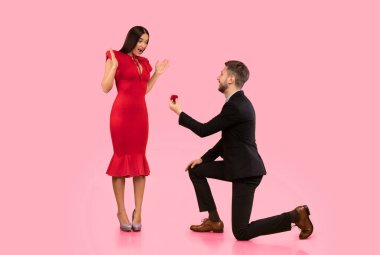 Teklif. Sevecen Adam Sürpriz Kız Arkadaşı Nişan Yüzüğü Tekrarı Sarı Stüdyo Arkaplanının Üzerinde Tek Diz Üzerinde Durmakta