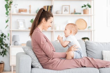 Sevgi dolu bir aile. Anne ve küçük bebeği evde oynuyorlar, boş alanla yan yana.