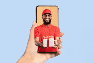 Hediye Teslimatı Uygulaması. Akıllı Telefon Ekranında Afro-Amerikan Kurye Adam Pembe Stüdyo Arkaplanından Müşteriye Paket Veriyor, Kameraya Gülümsüyor