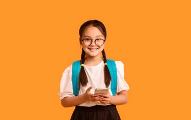 Neşeli Çinli Öğrenci Kız Cep Telefonu Kullanıyor Kameraya Gülümsüyor Sarı Arkaplanda Duruyor. Stüdyo Çekimi