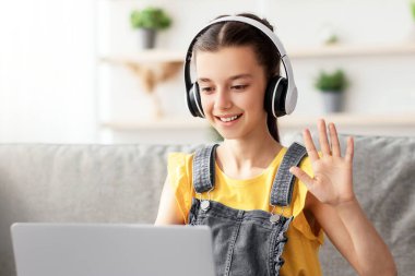 Çevrimiçi Video Çağrısı, Uzaktan İletişim. Masadaki koltukta oturmuş bilgisayarla sanal konferans yapan neşeli ergen öğrencinin portresi web kamerası selamlama öğretmenine ve sınıf arkadaşlarına el sallıyor.