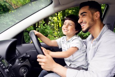 Şirin küçük çocuk ve genç Arap babası birlikte arabaya biniyorlar, küçük erkek çocuk babalarının kucağında oturuyor, Orta Doğulu babaya ilgi gösteriyor, mutlu çocuğa araba sürmeyi öğretiyor, yandan bakmayı öğretiyor.