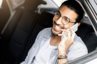 Taksinin arka koltuğunda oturan neşeli, genç Hintli adam, cep telefonuyla arkadaşlarıyla konuşuyor ve gülümsüyor, pencereden vuruluyor, fotokopi çekiyor. Ulaşım hizmeti kullanan yakışıklı, uzun saçlı bir Arap.