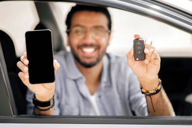 Otomatik araba anahtarına ve akıllı telefona odaklanın. Orta doğulu erkeklerin elinde boş ekranlı, neşeli Hintli adam araba kiralama, kiralama, cep telefonu satın alma, taklit etme için mobil uygulama gösteriyor.