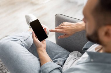 Evde boş ekranı olan akıllı telefonu kullanan tanınmayan genç adam, web sitesi ya da mobil uygulama tasarımı için model. Milenyum insanının elinde modern aletler, reklam için yer tutarken yakın plan.
