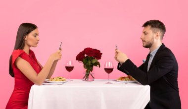 Sıkıcı randevu. Akşam yemeği sırasında cep telefonu kullanan çift stüdyoda sarı arkaplan pozu veriyor..