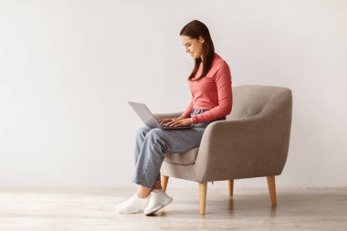 Mutlu genç bayan koltukta oturuyor, dizüstü bilgisayar kullanıyor, uzaktan çalışıyor ya da iş görüşmesi yapıyor, boş yer var. Milenyum Kafkasyalı kadın online ders alıyor ya da webinar seyrediyor