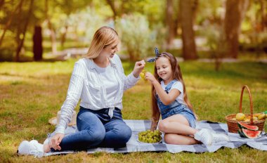 Piknik konsepti. Neşeli Anne ve Kız Üzüm Yiyerek Parkta Oturarak Rahatlıyor.