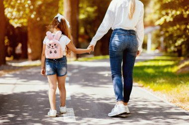 Tanımlanamayan anne ve küçük kızı dışarıda el ele tutuşuyorlar. Aile Yürüyüşü Konsepti. Kırpılmış, Arka Görünüm